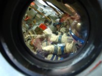 This picture through the window of the Soyuz simulator shows Yuri using his pointer to activate systems on the control panel. Because the design of the cockpit requires the commander to be slightly lower than the other crew members, he can't reach the control panel without the stick.