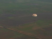 The capsule with it's parachute cannot be missed against the flat open terrain of the landing site.